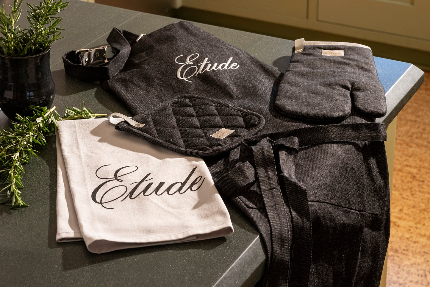 Black Etude apron, oven mitt, and tea towel with "Etude" embroidered. 